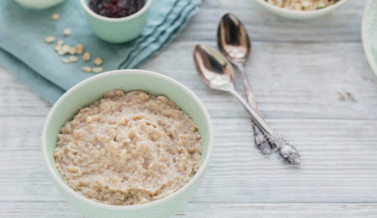 Oatmeal porridge bowl with berry jam on the white wooden background. Healthy nutritious breakfast.