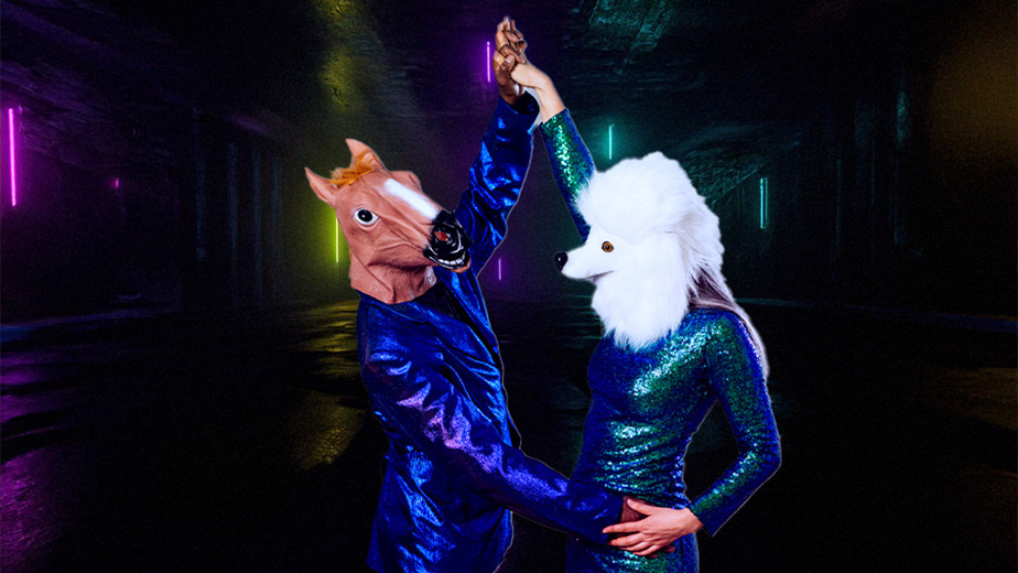 a picture of a man in a horse mask, with a woman in a poodle mask dancing