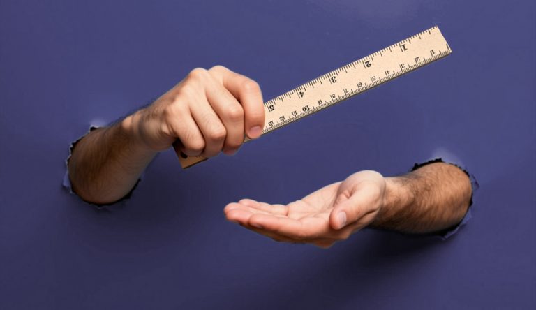 an image of two arms stuck through holes in a paper background, the hands are holding a ruler
