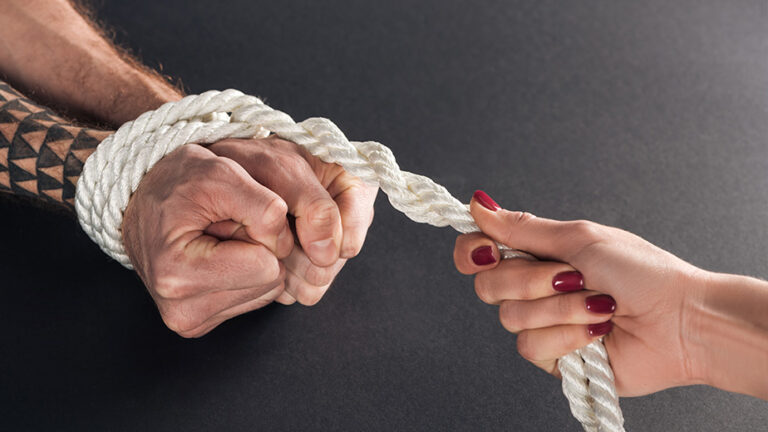 a man's hands bound by white rope, that's being held by a woman's hands