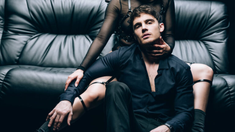 A woman sitting on a sofa with a man between her knees sitting on the floor